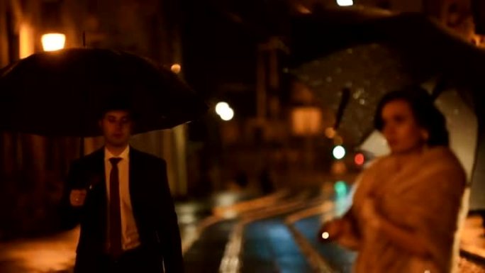 美丽的黑色风格夫妇在夜城街上的雨中相遇，躲在雨伞下躲避雨水。时尚男人亲吻华丽的女士