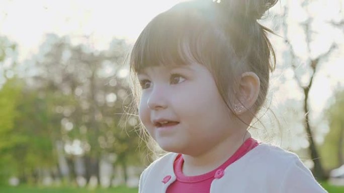 可爱的小女孩在阳光明媚的春天公园对着镜头微笑