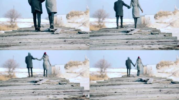 年轻漂亮的夫妇穿着外套，走在木板桥上，绕着雪走。
