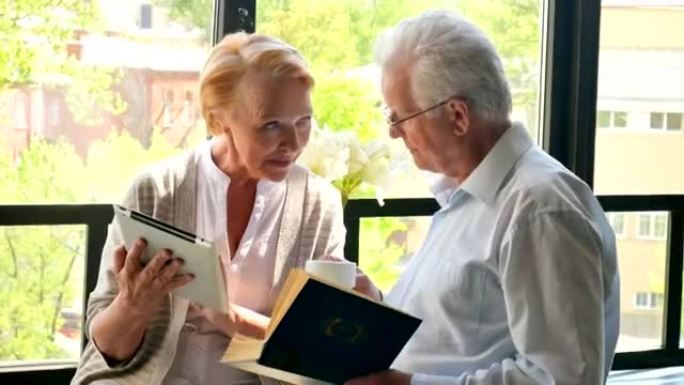 幸福可爱的退休夫妇站在一起，平板电脑和书。他们微笑
