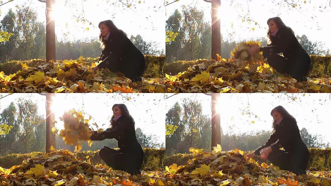 一个女孩从秋天公园的树枝上扔黄色的叶子