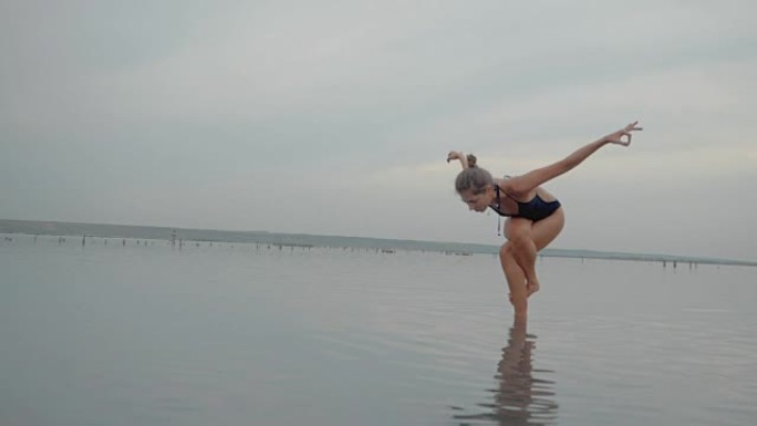 穿着泳衣的年轻白人妇女在水里曼，湖或河里练习瑜伽。美丽的倒影。复杂的体式，平衡。健身、运动、瑜伽和健