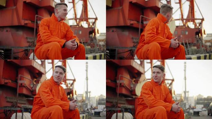 一个穿着橙色制服的年轻人在休息时坐在港口的海边