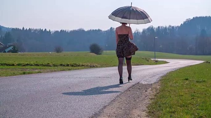 在阳光明媚的日子里，美丽的女人在乡村中间的路边散步，镜头是慢动作拍摄的。
