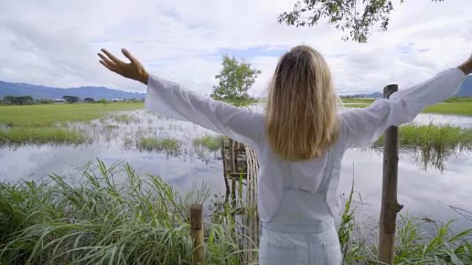 亚洲旅行的年轻女子双臂伸出湖面，年轻女子站在湖边双臂张开