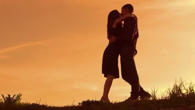 日落时一对夫妇的剪影。日落慢动作中的男人和女人剪影。恋爱中的情侣在日出时接吻。男人和女孩拥抱剪影家庭