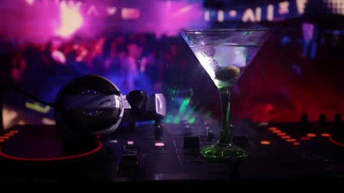 夜总会dj控制器上配有马提尼酒和橄榄的玻璃杯。带迪斯科灯的夜总会音乐派对上俱乐部饮料的Dj控制台