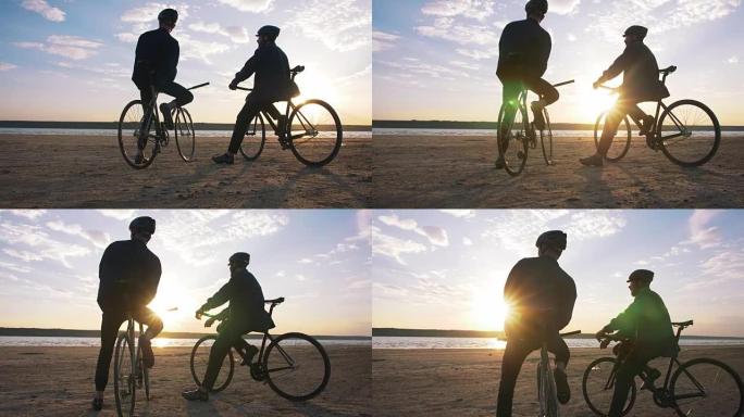 两个年轻人坐在沙滩上的自行车上，以橙色的日落天空为背景