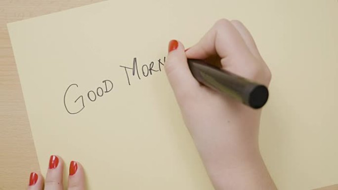 年轻的女性双手写着早安，用黑色记号笔在黄纸上画笑脸