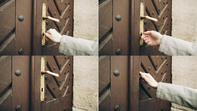 女性用旧钥匙打开旧门。用手将古董铁钥匙放入门锁中，然后用手转动钥匙。