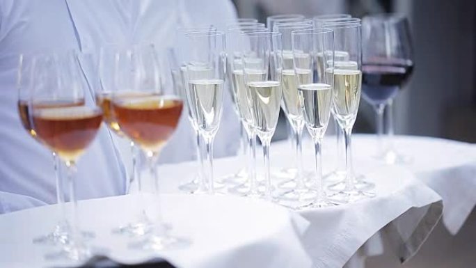 服务员用酒精饮料迎接客人。香槟、红酒、白葡萄酒放在托盘上。
