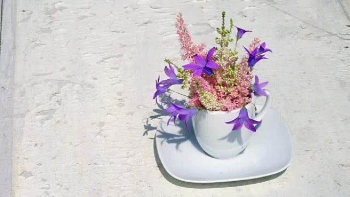 Astilba和蓝色铃铛花束在白色咖啡杯中，花瓶在风中生长在旧的白色背景上，为您的文本提供复制空间