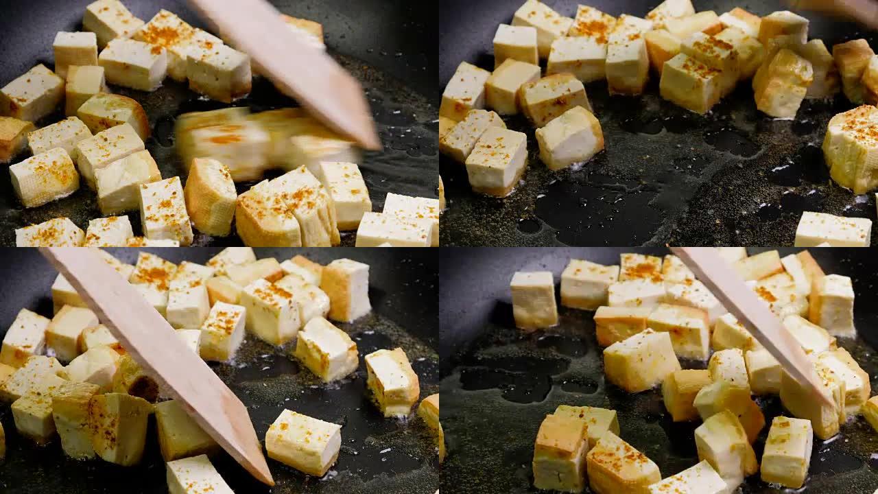 在铸铁锅上炒香料豆腐，是烹饪素食素食的健康成分。黑色背景上的油炸豆腐。