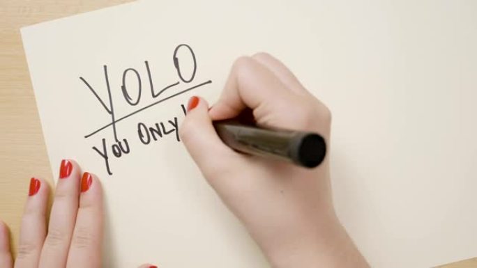 十几岁的女性手用红色指甲油书写yolo你只活一次激励引用在一张带有黑色记号笔的白纸上