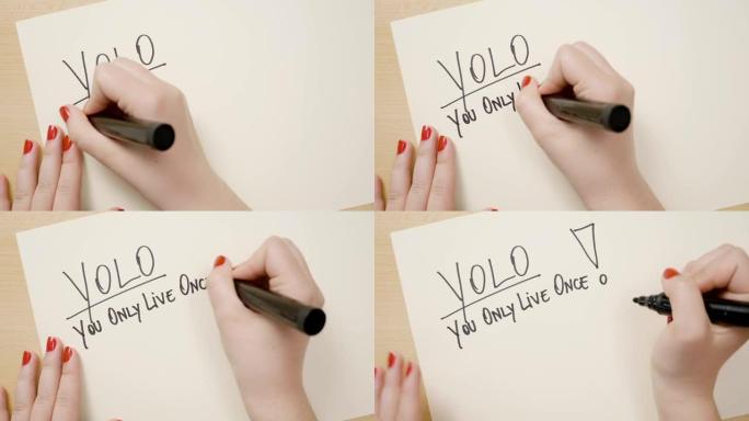 十几岁的女性手用红色指甲油书写yolo你只活一次激励引用在一张带有黑色记号笔的白纸上