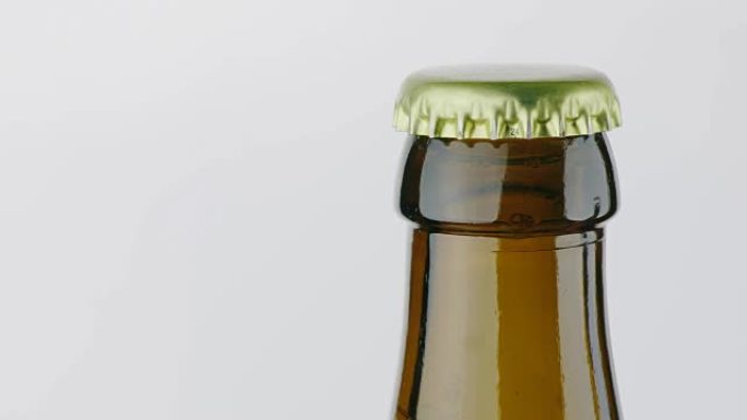 一瓶啤酒的脖子上盖着一个金属盖子。在白色背景上