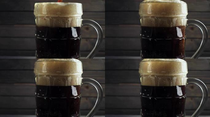 将冷的黑啤酒倒入啤酒杯中。在深色木质背景上。慢动作