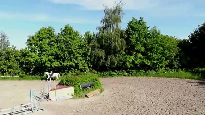 从上方观看，空中视频拍摄，训练沙场，游乐场，骑手，骑师骑马，与马一起进行各种练习，在障碍物旁边。夏天