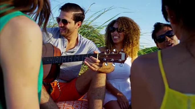 多民族的人带着吉他享受海滩野餐