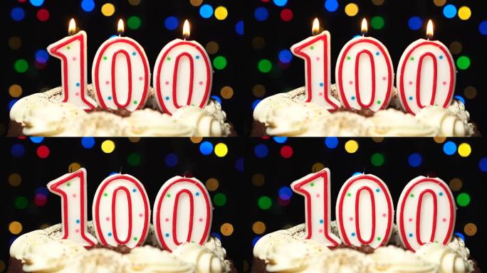 蛋糕顶部的数字100-100生日蜡烛燃烧-最后吹出来。彩色模糊背景