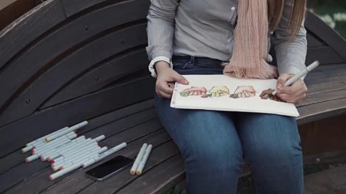 一个女人的手的特写，谁坐在一个长凳上，在一本相册中画标记