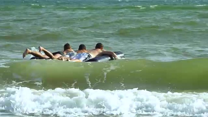 男人在充气床垫上在海里游泳。他们在笑。床垫在海浪上折腾。
