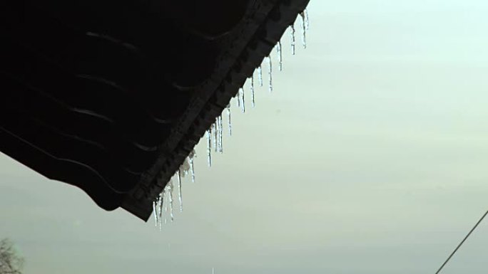 冬天天空景观边缘屋顶上挂着的融化冰柱。在春季景观上从闪亮和融化的冰柱中偷听