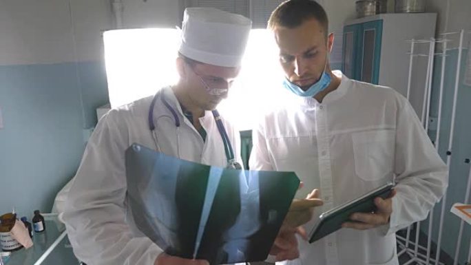 男性医生使用平板电脑，同时互相咨询患者的x射线图像。医院的医务人员检查x射线照片。两名高加索医生看着