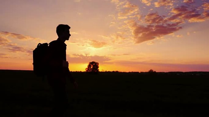 一个背着背包的少年在田野或乡村走向日落。侧影视频，侧视图。概念-新的研究，前进到未知，离开家