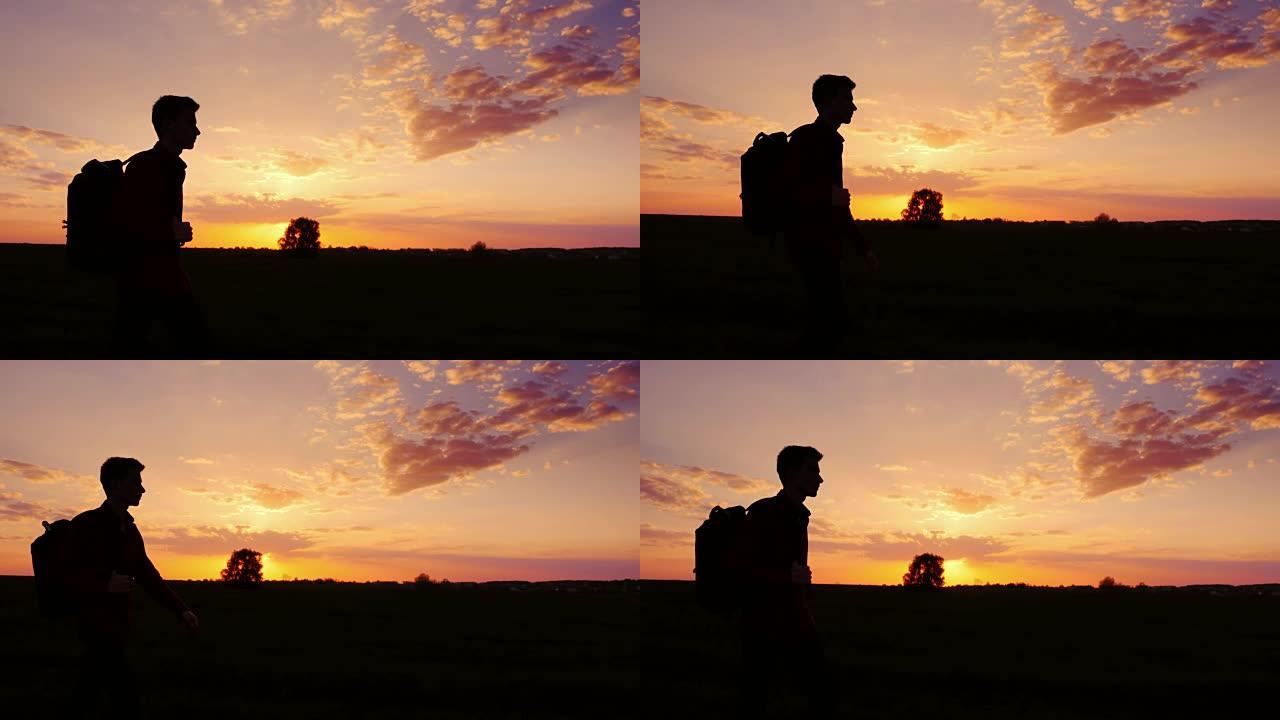 一个背着背包的少年在田野或乡村走向日落。侧影视频，侧视图。概念-新的研究，前进到未知，离开家