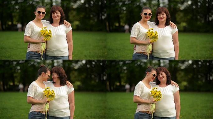 公园里一个微笑的成熟女人和成年女儿的肖像。他们正在庆祝母亲节。绿草在背景上