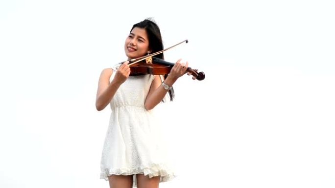 年轻漂亮的亚洲女孩穿着连衣裙拉小提琴呆在海滩上