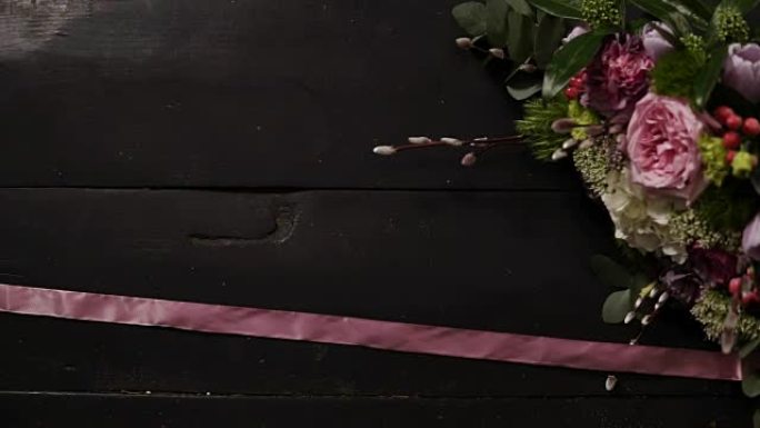 两条丝质粉红丝带在黑暗的木质表面蔓延开来，一束美丽的鲜花插在一个框架里。慢动作