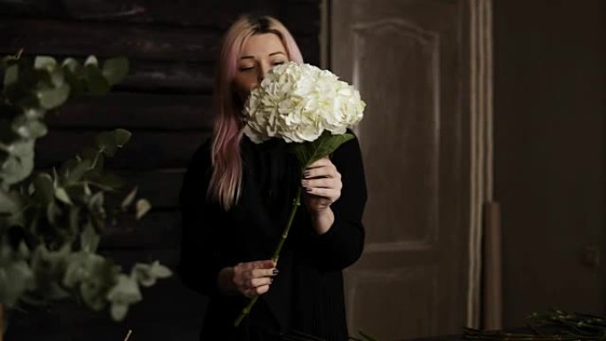 粉红色头发美丽的花店手里拿着巨大的白色绣球花。摘下多余的叶子