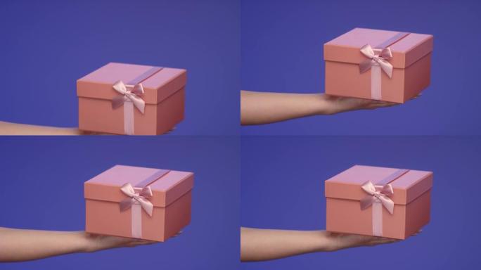 女人手里拿着蓝色屏幕上的粉红色礼品盒; 庆祝概念