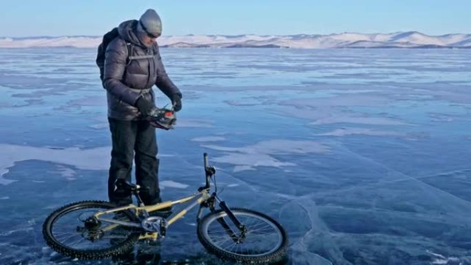 男人和他的自行车在冰上。骑自行车的人穿着灰色羽绒服，背包和头盔。冰冻的贝加尔湖的冰。自行车上的轮胎上