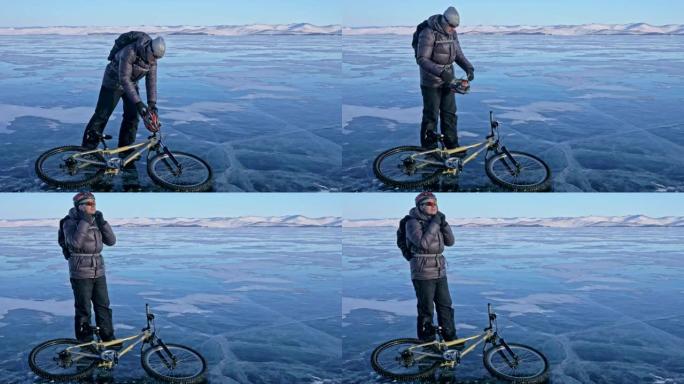 男人和他的自行车在冰上。骑自行车的人穿着灰色羽绒服，背包和头盔。冰冻的贝加尔湖的冰。自行车上的轮胎上