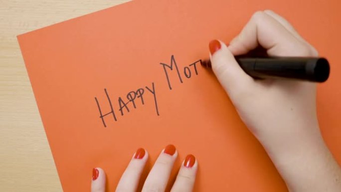 一个年轻女孩女儿的手用黑色记号笔在红纸上写下母亲节快乐
