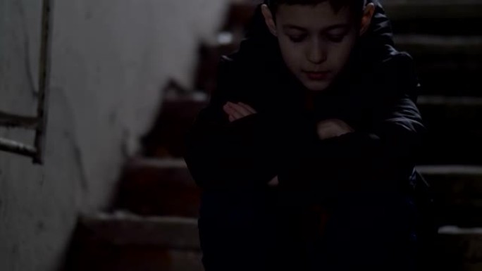 男孩独自一人坐在破旧的拆迁房屋中，对事件感到遗憾，天气寒冷