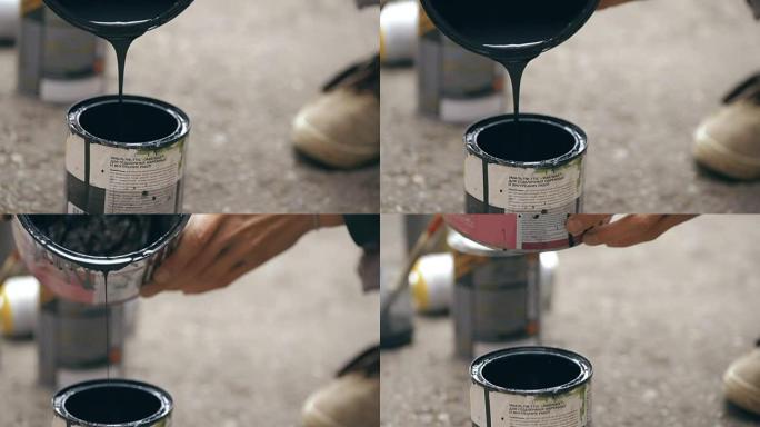 艺术家将黑色油漆从罐倒在另一个罐中。