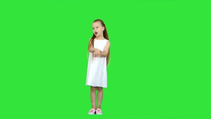 年轻的女士穿着可爱的连衣裙和白鞋，在绿色屏幕上唱着一首歌，色键