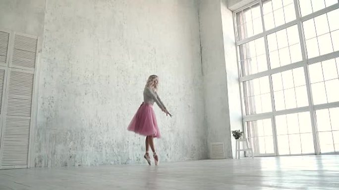 女孩在一扇巨大窗户的背景下跳舞。芭蕾舞演员在工作室表演旋转木马。经典芭蕾舞短裙和尖角芭蕾舞演员