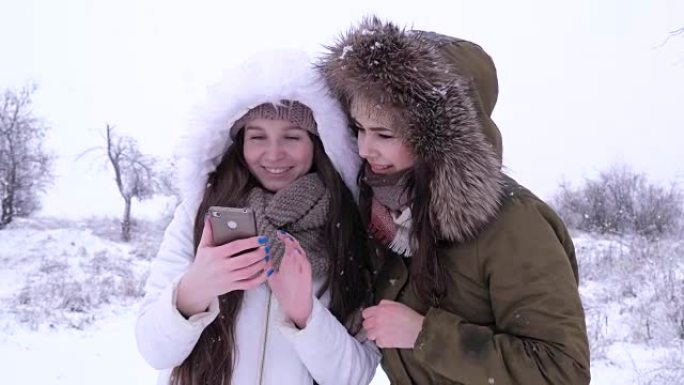 笑的女孩在冬天雪花飘落的背景下在小工具上观看图片