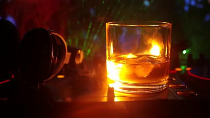 夜总会dj控制器上的玻璃和带冰块的威士忌。Dj耳机在夜总会的音乐派对上戴一杯whilsky，配有迪斯