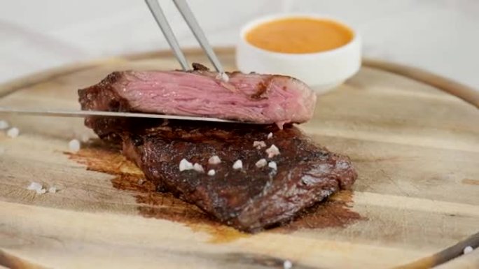 餐馆里的那个人用刀切了大理石牛肉牛排，烤了。在木板上服务。在厨房烹饪牛排。新鲜、美味、辛辣、多汁的肉
