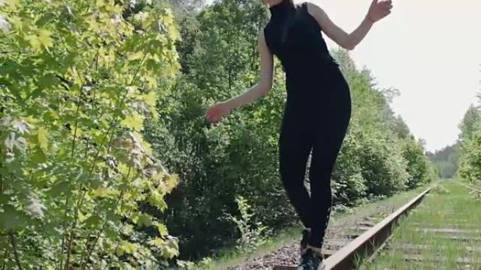 穿着黑色西装的年轻黑发女人在旧铁路的铁轨上。保持平衡的女孩