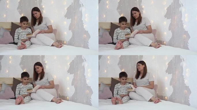 一个穿着睡衣的漂亮女孩在睡觉前坐在床上给一个小男孩看书。总体规划。高清