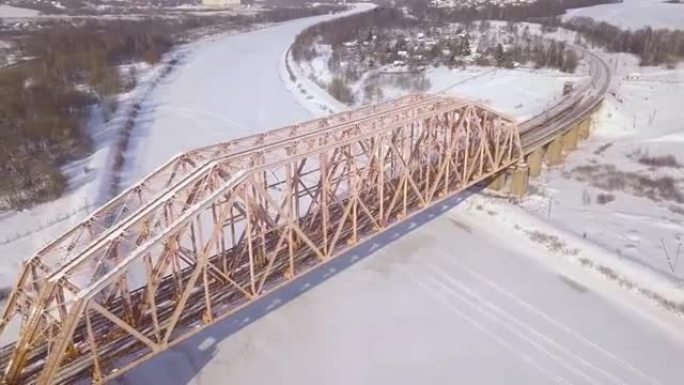 铁路桥梁和铁路轨道，用于冬季景观无人机视图中冰冻河流上的火车交通。悬吊火车桥通过河流和汽车高速公路鸟