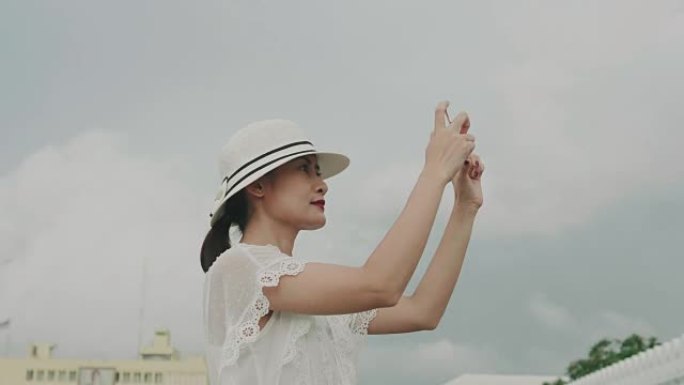 年轻女性游客穿着别致的复古连衣裙，在泰国巴格纳克寺庙观光时用智能手机拍照