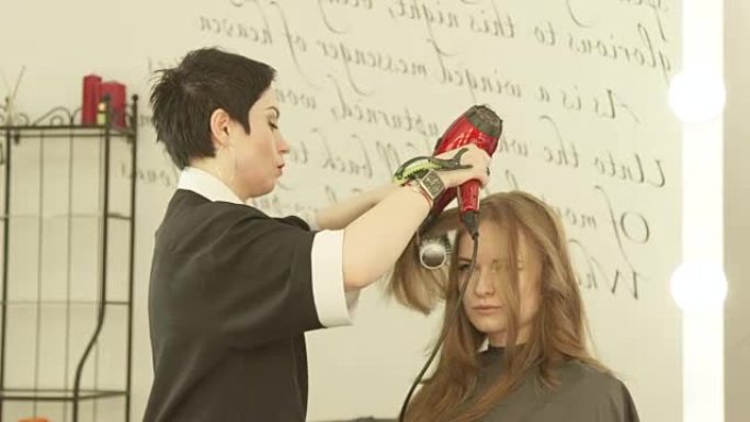 在美发沙龙用吹风机和发刷对长发进行发型设计的活跃女性。在美容院清洗和切割后，用吹风机和梳子关闭理发器